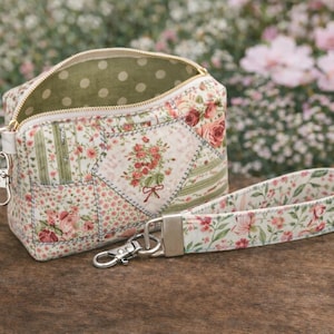 Può includere: Un beauty case con stampa floreale e cinturino da polso abbinato. La borsa presenta un design patchwork con rose e altri fiori nei toni del rosa, verde e crema. La fodera interna è verde oliva con pois bianchi.