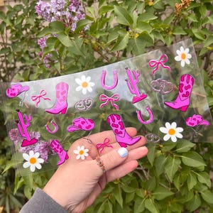 May include: A sheet of pink and white stickers featuring cowboy boots, horseshoes, cacti, hearts, and daisies.