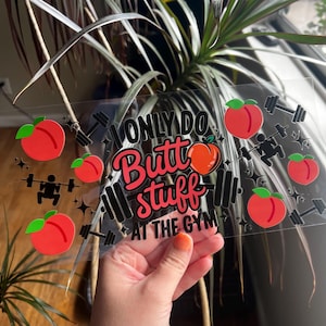 Puede incluir: Una pegatina transparente con el texto "ONLY DO Butt stuff AT THE GYM" en negro y rosa. La pegatina presenta gráficos de melocotones rojos con hojas verdes y gráficos de pesas y halterofilia negros.