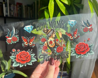 May include: Clear sticker sheet with a design featuring a woman with tattoos, roses, butterflies, diamonds, and the text "Cool Moms Have Tattoos". The design is in red, black, and blue.