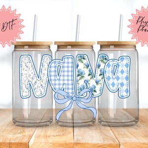 May include: Three clear glass tumblers with wooden lids and straws. Each tumbler features the word "Nana" in a different blue pattern: floral, gingham, and argyle. A blue bow is centered below the word. The words "UV DTF" and "Physical Product" are in pink starbursts.