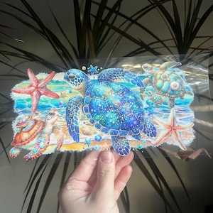 May include: A colorful illustration featuring several sea turtles of varying sizes, along with starfish and seashells. The turtles have blue and turquoise shells, and the scene depicts a beach with ocean waves. The artwork is vibrant and detailed.