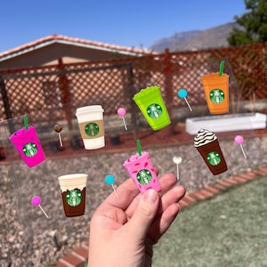 May include: A sheet of clear stickers featuring various colorful coffee drinks with a cartoon woman's face on each. The stickers are on a clear background and are ready to be applied to a surface.
