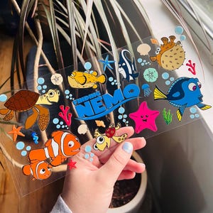 Puede incluir: Una hoja transparente de pegatinas con personajes de la película Buscando a Nemo. Las pegatinas incluyen a Nemo, Dory, Marlin, Crush y otros personajes. Las pegatinas son perfectas para añadir un toque de diversión a cualquier proyecto.