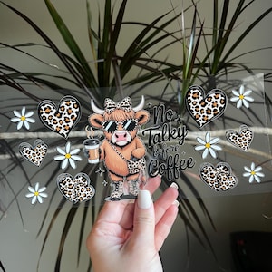 May include: A clear sheet featuring a cartoon cow wearing sunglasses, a bow, and a leopard print purse and boots, holding a coffee cup. The text "No Talky before Coffee" is also present, along with leopard print hearts and white daisies.