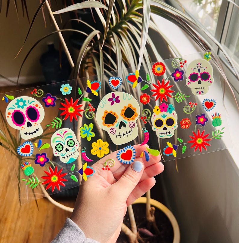 Puede incluir: Una hoja de pegatinas coloridas con tem&aacute;tica del D&iacute;a de Muertos con calaveras de az&uacute;car, flores y otros dise&ntilde;os festivos. Las pegatinas son perfectas para agregar un toque de cultura mexicana a tus manualidades, diarios o decoraci&oacute;n del hogar.