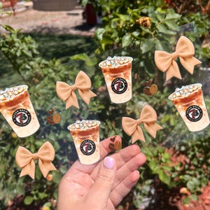 Könnte beinhalten: Eine Folie mit transparenten Aufklebern, die eisgekühlte Kaffeegetränke mit dem Text "Seven Brew Coffee" und braunen Schleifen zeigt.