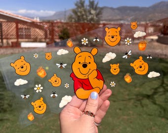 May include: A clear sheet of Winnie the Pooh stickers with various images of Winnie the Pooh, honey pots, bees, and clouds. The stickers are on a white background.