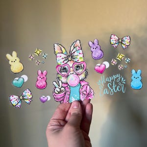 Puede incluir: Ilustración colorida de Pascua con un conejito con gafas de corazón y una burbuja de chicle. Incluye Peeps, lazos, corazones y el texto "Happy Easter".
