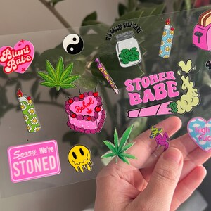 Może przedstawiać: Arkusz r&oacute;żowych i zielonych naklejek z r&oacute;żnymi wzorami, w tym blunt, joint, upieczony tort, zapalniczka, liść i tekst "Blunt Babe", "Stoner Babe", "Sorry We're Stoned", "It's Called Self Care", "420" i "High as Fuck".