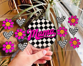 Puede incluir: Una hoja de pegatinas de vinilo transparente con un círculo a cuadros blanco y negro con la palabra "Mama" en escritura rosa. También hay pegatinas de flores rosas con caras sonrientes amarillas, corazones rosas con patrones de cuadros blanco y negro, y corazones rosas con patrones de cuadros blanco y negro.