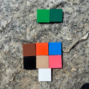 Puede incluir: Un conjunto de nueve bloques peque&ntilde;os, cuadrados y de colores. Los bloques est&aacute;n dispuestos en una cuadr&iacute;cula. Los colores son marr&oacute;n, naranja, azul, negro, beige, rosa, blanco, verde y verde oscuro.