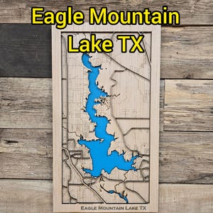 Puede incluir: Un mapa de madera del lago Eagle Mountain en Texas, con el área del lago resaltada en azul. El mapa está enmarcado y montado sobre un fondo de madera. El texto en la parte superior dice "Eagle Mountain Lake TX".