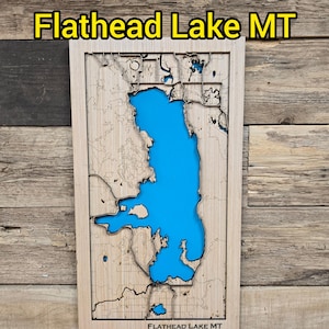 May include: Wooden map of Flathead Lake, Montana, with a vibrant blue lake and detailed land contours. The text "Flathead Lake MT" is displayed at the top. The map is set against a rustic wooden background.