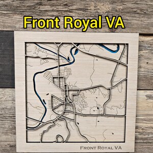 May include: Wooden map of Front Royal, VA, with a detailed laser-cut design. The map features the city's layout, including roads and waterways, with the text "Front Royal VA" at the top and bottom. The map is set against a wooden background.