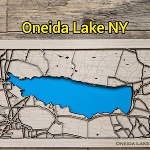 Könnte beinhalten: Eine Holzkarte des Oneida Lake, NY, mit einem blauen See und detaillierten, lasergeschnittenen Straßen und Landmerkmalen. Der Text "Oneida Lake NY" wird oben und unten im Rahmen in Gelb angezeigt. Die Karte befindet sich vor einem Holzmaserungshintergrund.