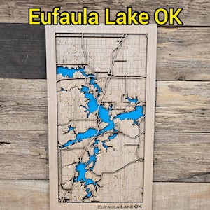 May include: A wooden map of Eufaula Lake, OK, with the lake's water areas filled with blue resin. The map is framed and mounted on a wooden background. The text "Eufaula Lake OK" is displayed at the top.