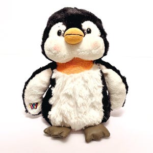 May include: A plush penguin toy with a black head and back, white chest and belly, and orange accents. The penguin has a yellow beak, pink cheeks, and brown feet. A small patch with a "W" logo is visible on the left side. The toy is designed to be soft and cuddly.