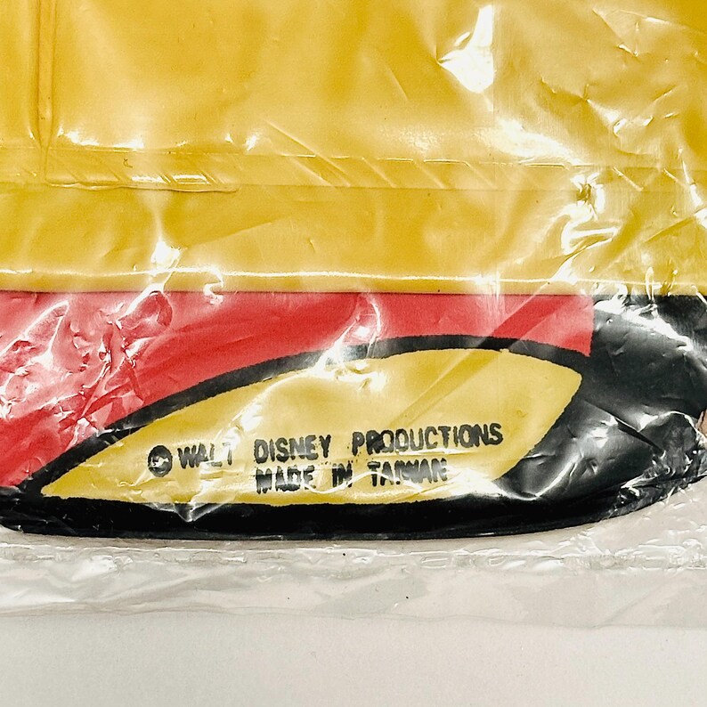 K&ouml;nnte beinhalten: Nahaufnahme eines gelben, roten und schwarzen Mickey-Maus-Charakters aus Plastik. Der Charakter tr&auml;gt einen roten Hut und hat einen schwarzen Umriss. Der Text "&copy; WALT DISNEY PRODUCTIONS MADE IN TAIWAN" ist auf der Unterseite des Charakters aufgedruckt.