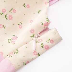 May include: Close-up of a pink and white floral print dress with a zipper detail. The dress has a pink trim and a white background with small pink flowers.