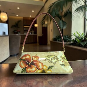 Puede incluir: Un bolso rectangular con asa marr&oacute;n y herrajes dorados. El bolso presenta un estampado floral con una gran flor de hibisco naranja y flores amarillas. El fondo tiene un dise&ntilde;o de mapa.
