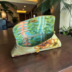 Puede incluir: Bolso de mano beige con estampado floral tropical con flores naranjas y amarillas. El interior tiene un estampado floral azul y verde. El bolso de mano est&aacute; abierto, revelando una cremallera dorada y un cierre dorado.
