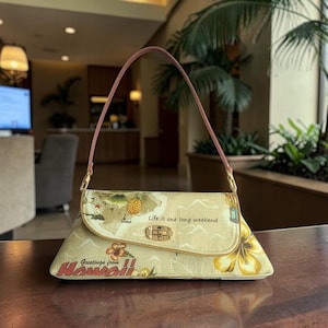 Puede incluir: Bolso beige con estampado de mapa y flores, asa rosa y cierre dorado. El bolso tiene el texto "Life is one long weekend" y "Greetings from Hawaii!!".
