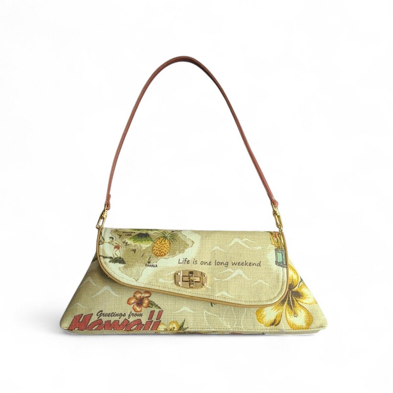 Puede incluir: Un bolso de mano beige con un asa marr&oacute;n. El bolso presenta un dise&ntilde;o de mapa con pi&ntilde;as, flores y el texto "Greetings from Hawaii" y "Life is one long weekend."