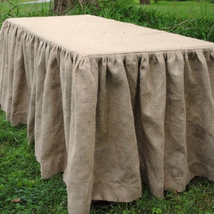 Puede incluir: Una falda de mesa de arpillera marrón con un borde fruncido. La falda está drapeada sobre una mesa y está sentada sobre una superficie de hierba verde.