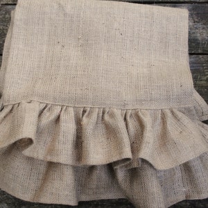May include: A brown burlap table runner with a double layer of ruffles around the bottom edge.