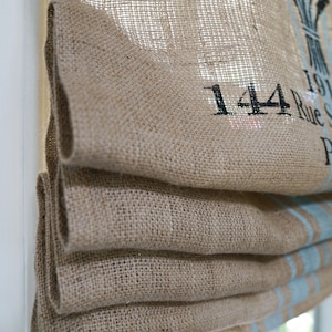 May include: A brown burlap roman shade with a blue and white stripe pattern. The shade has the text "144 Rue S" printed on it.