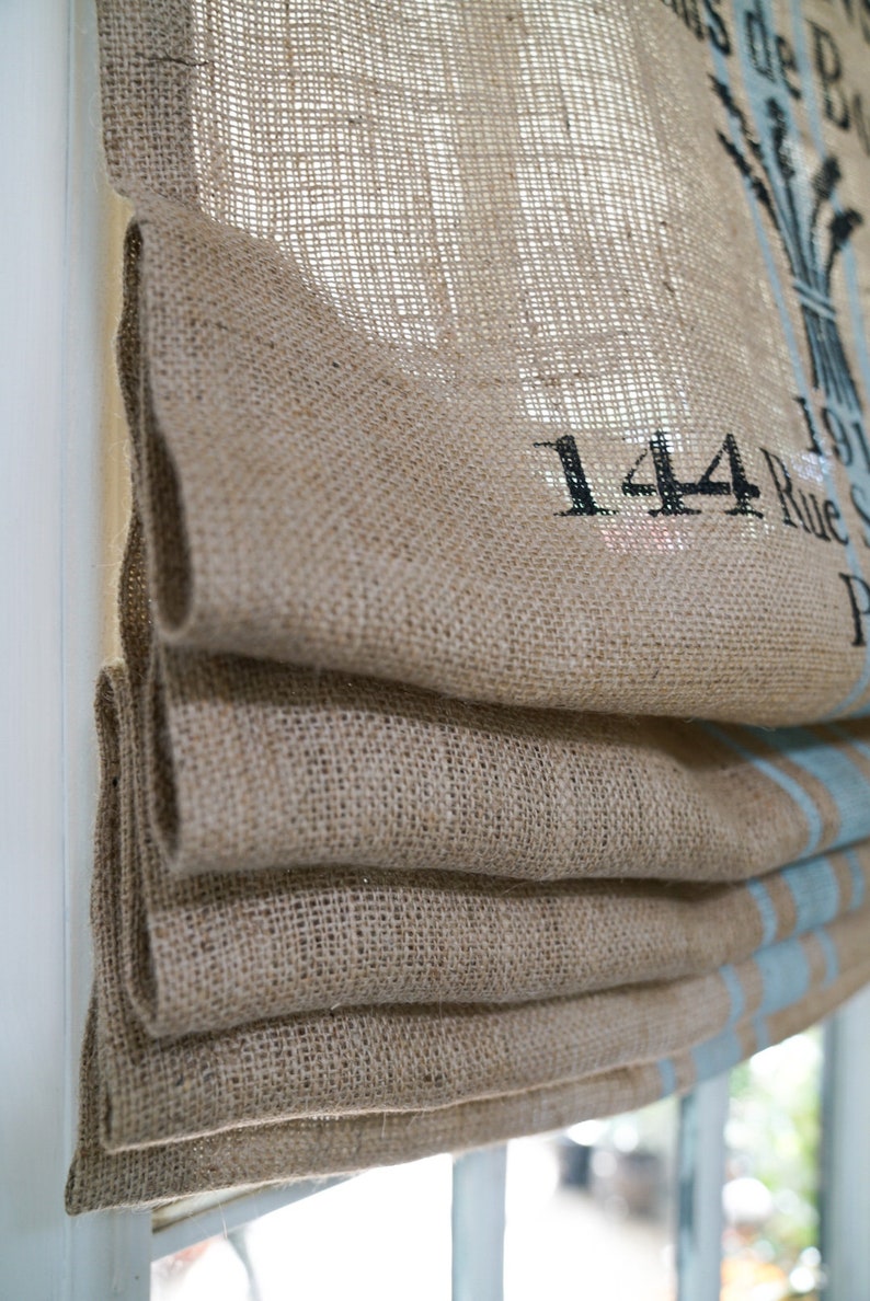 May include: A brown burlap roman shade with a blue and white stripe pattern. The shade has the text "144 Rue S" printed on it.