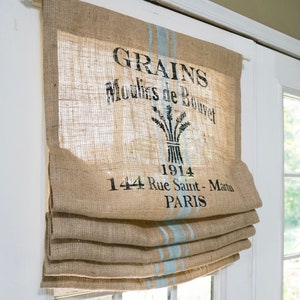 May include: A burlap roman shade with blue stripes and a vintage French grain sack design. The design includes the text "GRAINS Moulins de Bouvet 1914 144 Rue Saint - Martin PARIS".