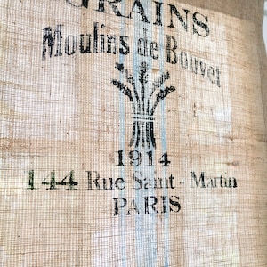 May include: A burlap sack with blue stripes and black text that reads "GRAINS Moulins de Bouvet 1914 144 Rue Saint-Martin PARIS".