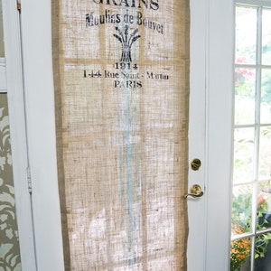 May include: A burlap curtain with a vintage design featuring the text "GRAINS Moulins de Bouvet 1914 1-44 Rue Saint-Martin PARIS". The curtain has a blue and white striped pattern.