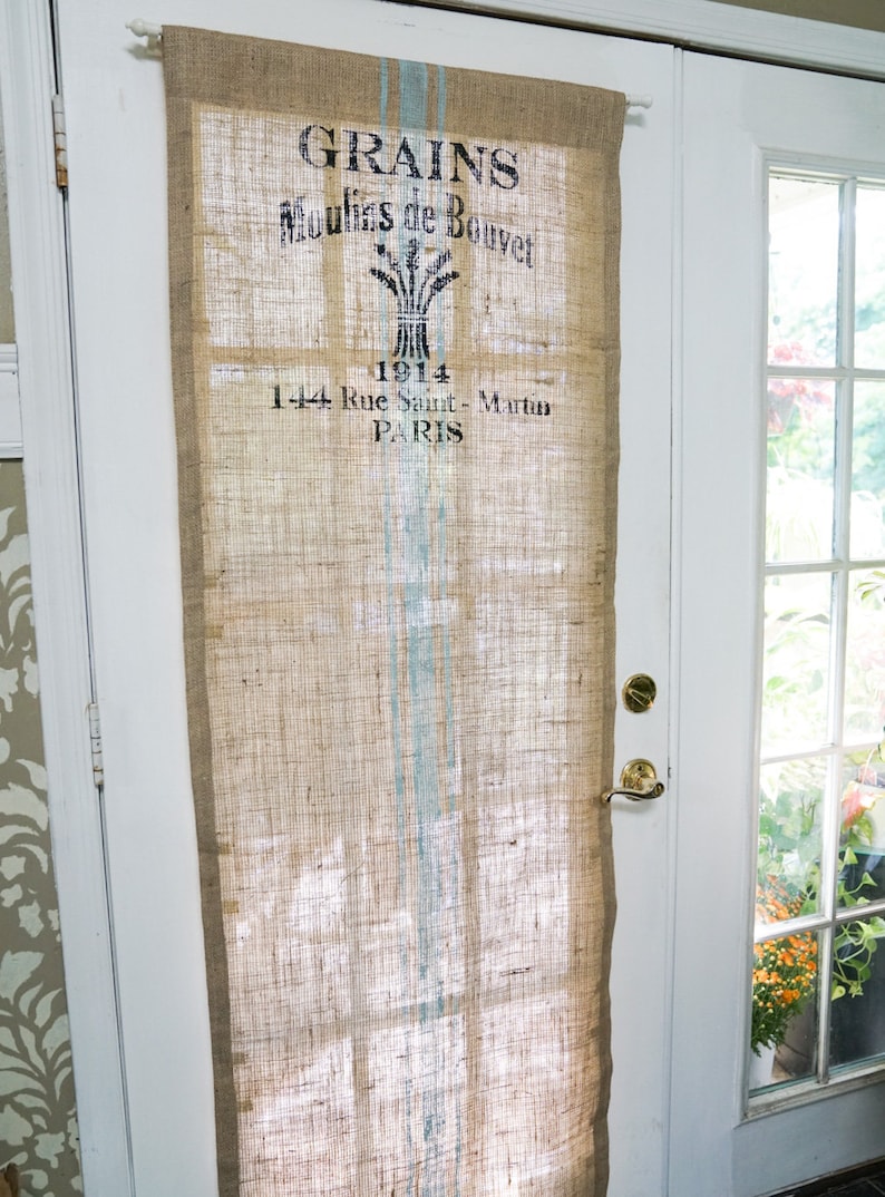 May include: A burlap curtain with a vintage design featuring the text "GRAINS Moulins de Bouvet 1914 1-44 Rue Saint-Martin PARIS". The curtain has a blue and white striped pattern.