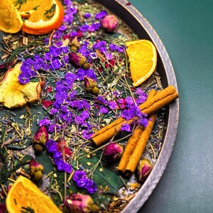May include: A wooden bowl filled with dried orange slices, cinnamon sticks, purple flowers, and dried rose buds.