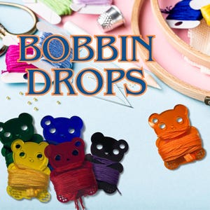 May include: Six colorful plastic bear-shaped bobbin thread holders with different colored threads wrapped around them. The text "Bobbin Drops" is displayed in large blue letters on a pink background.