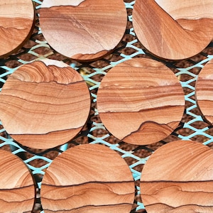 May include: Close-up of a pattern featuring circular, reddish-brown stone pieces. The stones have natural, layered textures and are set within a light blue, crisscross metal framework. The overall design suggests a natural, earthy aesthetic.