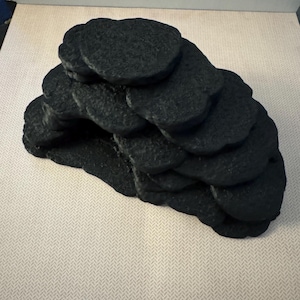 May include: A black, layered, organic-shaped sculpture. The object appears to be made of a textured material, possibly stone or a similar substance. The form is composed of several stacked, rounded elements.