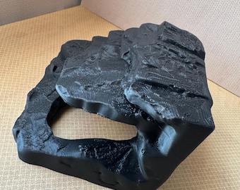 May include: A black, abstract sculpture with a textured surface and a large, irregular hole. The object has a rough, rocky appearance, suggesting a natural form. The sculpture is made of a solid, dark material.