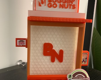 May include: A 3D printed model of a store front with the words "Buggin' Go Nuts" on the sign. The store is orange and white with a "BN" logo on the front. There is a sticker on the bottom right corner that says "Buggin' Go Nuts" with the text "America Runs From Nuts".
