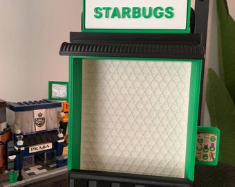 May include: A 3D printed model of a Starbucks store, featuring a green star with a black logo, a black and white sign that reads "STARBUGS", and a green and black storefront with a white interior.