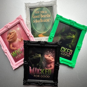 May include: Four framed art prints with fantasy-themed bearded dragon illustrations. One pink frame shows a dragon in a tutu with a wand. Another green frame shows a dragon in a witch hat. Text includes "Wicked for Good".