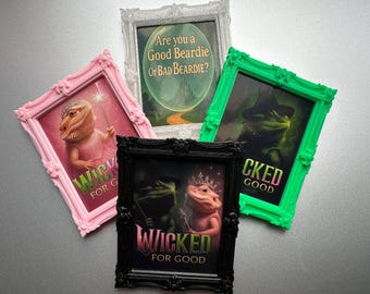 May include: Four framed art prints featuring bearded dragons in whimsical scenes. One pink frame has a dragon in a tutu with a wand. Another green frame shows a dragon in a witch hat. The text includes "Wicked for Good".