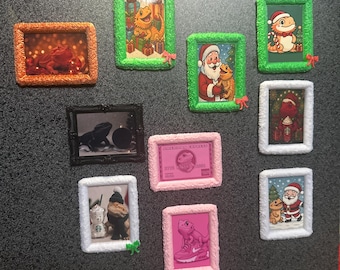 May include: A collection of framed art pieces featuring various images. The frames have textured edges in colors like green, orange, pink, and white. The images include a lizard, Santa Claus, and a Starbucks cup.