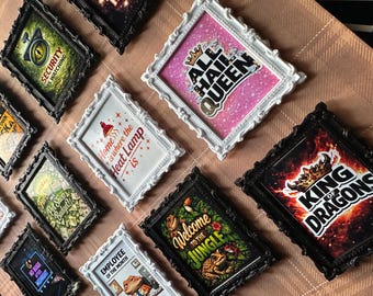 May include: Collection of framed art prints with various designs and text. Frames are black and white with ornate detailing. Prints include phrases like "All Hail Queen", "Welcome to the Jungle", and "King of Dragons".