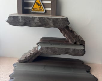May include: A multi-tiered reptile habitat with a wooden frame and textured, gray-brown platforms. A yellow triangle sign with a lizard graphic and the words "Reptile Zone" is attached to the top. The design mimics a natural rock formation.