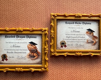 May include: Two framed diplomas, one for a Bearded Dragon and the other for a Leopard Gecko. Each features a reptile wearing a graduation cap. The diplomas are in ornate gold frames, set against a textured orange background.
