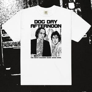 Pode incluir: Camiseta branca com um gráfico em preto e branco do filme "Dog Day Afternoon". O design inclui o título do filme e dois atores. O texto "THE MOST BIZARRE BANK SIEGE EVER" também está impresso.